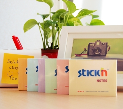 Eile sustatyti šeši gelsvi, rausvi, žalsvi, melsvi ir smėliniai Stick'n Notes blokai prie augalo ir fotoaparato nuotraukos