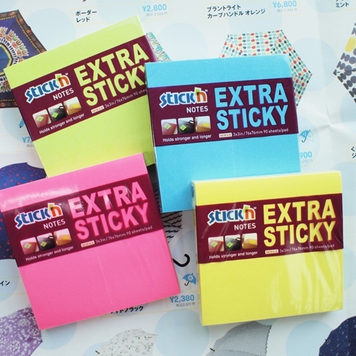 Žalias, mėlynas, rožinis ir geltonas Stick'N Extra Sticky lipniųjų lapelių blokeliai sudėti ant atversto katalogo