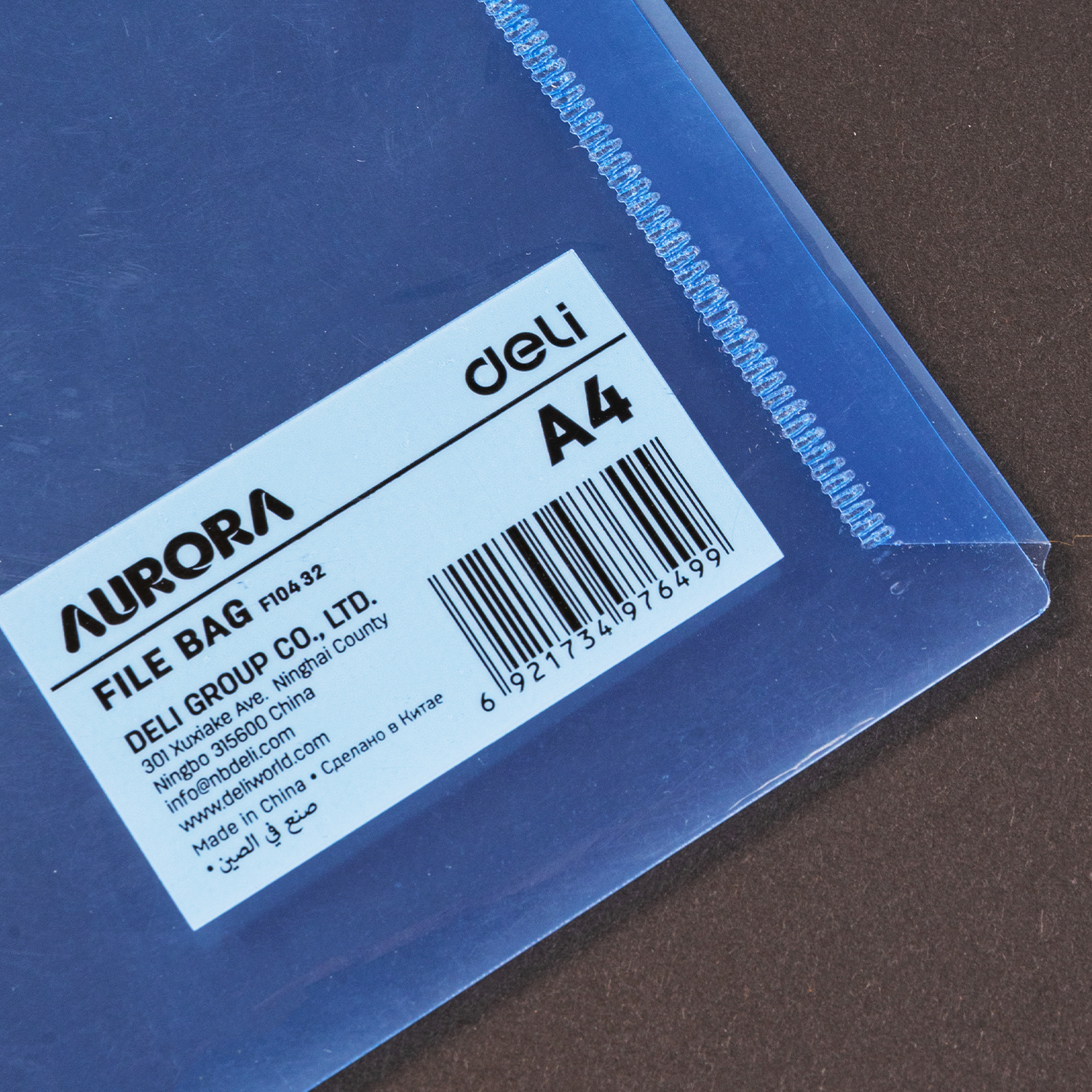 Mėlyno aplanko kampas ant rudo pagrindo su balta Aurora File Bag F104-32 Deli A4 etikete, barkodu ir dantyta siūle