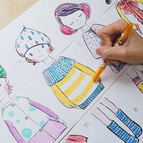 Ranka oranžiniu pieštuku spalvina Little Designer mergaitės megztinį šalia kitų spalvotų žiemos drabužių figūrų