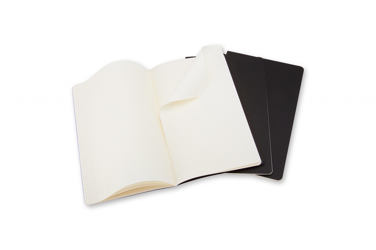 Atversta kreminiais linijuotais puslapiais Moleskine Cahier užrašinė ir dvi užverstos juodos užrašinės už jos