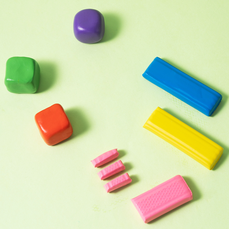 Žaliame fone išdėlioti violetinis, žalias, oranžinis, mėlynas, geltonas ir rausvas plastilinas